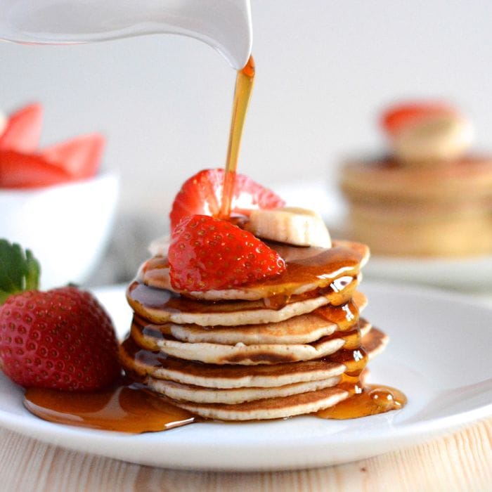 Maple syrup being poured onto a stack of American pancakes and running all over the plate.