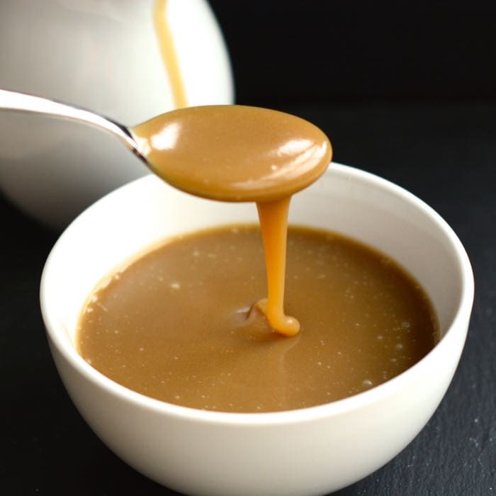A spoonful of caramel sauce drizzling down into a bowl of sauce.