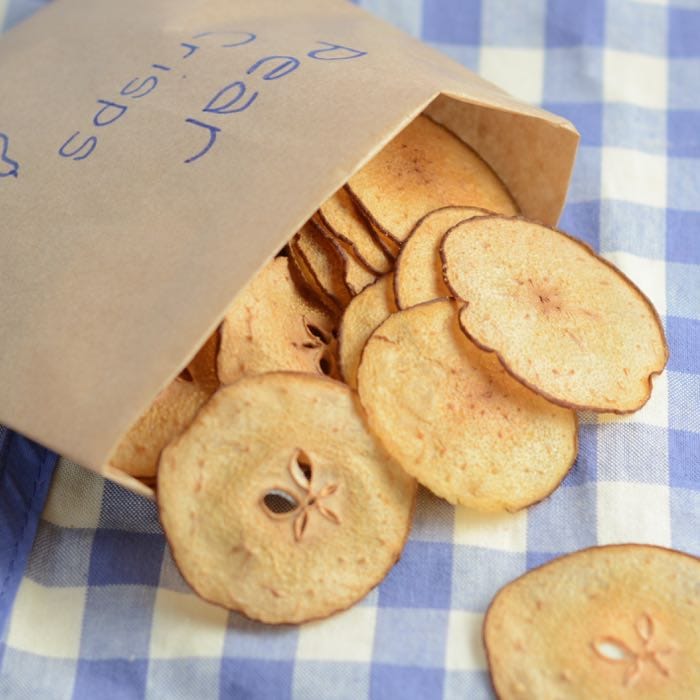 Pear crisps falling out of a homemade crisp packet on a blue and white checked cloth.