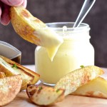 A potato wedges that just been dipped in mayonnaise. There's more wedges on a board and a jar of mayonnaise in the background.