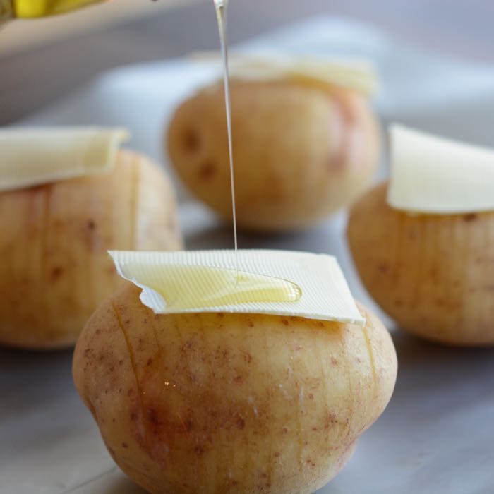 What hasselback potatoes look like before they're cooked. Potatoes with slits all the way along topped with butter and the drizzled with olive oil. 