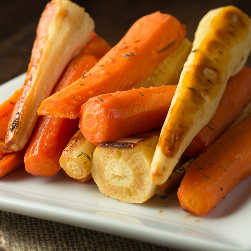 Cooked honey roasted carrots and parsnips stacked on a white plate.