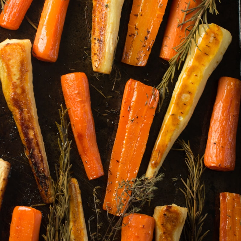 Cooked honey roasted carrots and parsnips on their baking tray shown from above. 