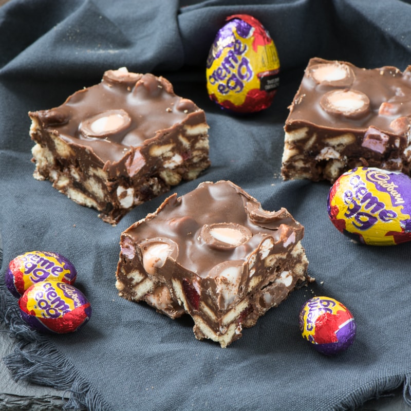Three pieces of Creme Egg rocky road surrounded by Creme Eggs in their wrappers.
