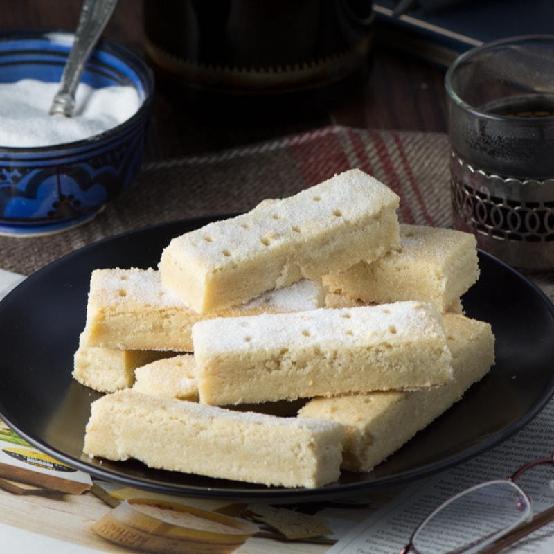 Ready to eat shortbread fingers shown from the side and stacked like jenga on a black plate.