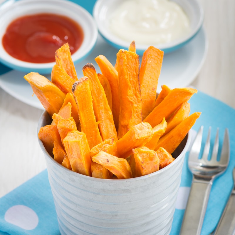Sweet Potato fries served on their end in a small metal pot with a fork and dipping sauces nearby. 