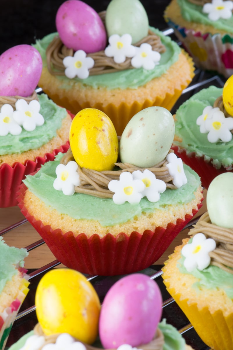 Close up of an easter nest cupcake with red case, white flowers and yellow and green mini eggs. 