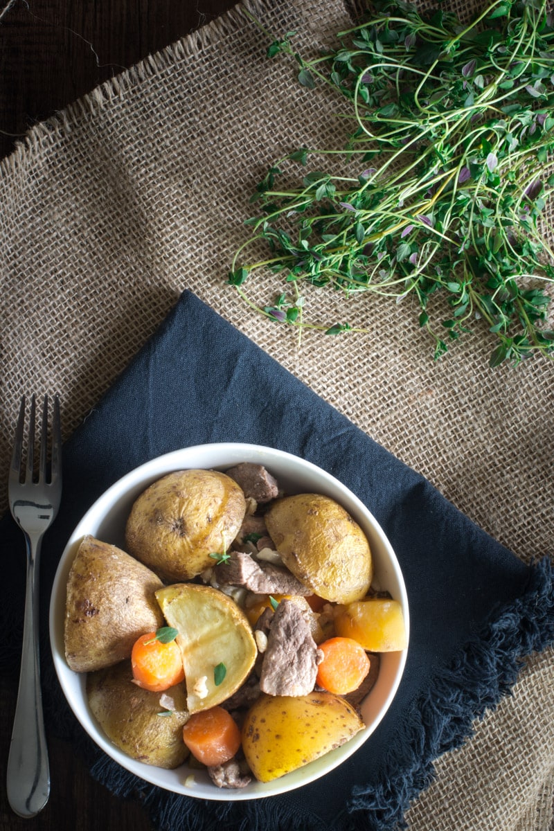 An overhead view of one serving of irish stew in a white bowl with a fork next to it. 