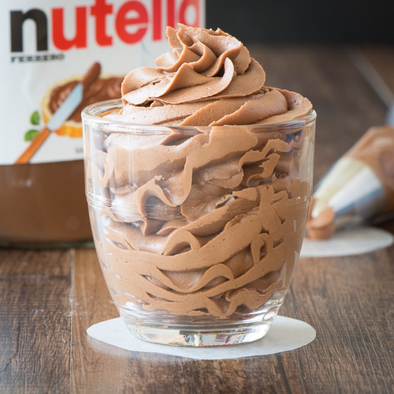 A glass full of piped Nutella buttercream with a jar of Nutella in the background.