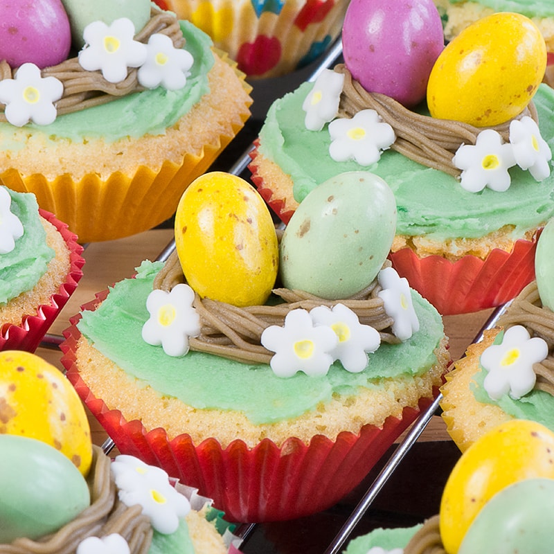 Close up on one easter nest cupcake in a red case surrounded by other cupcakes. 