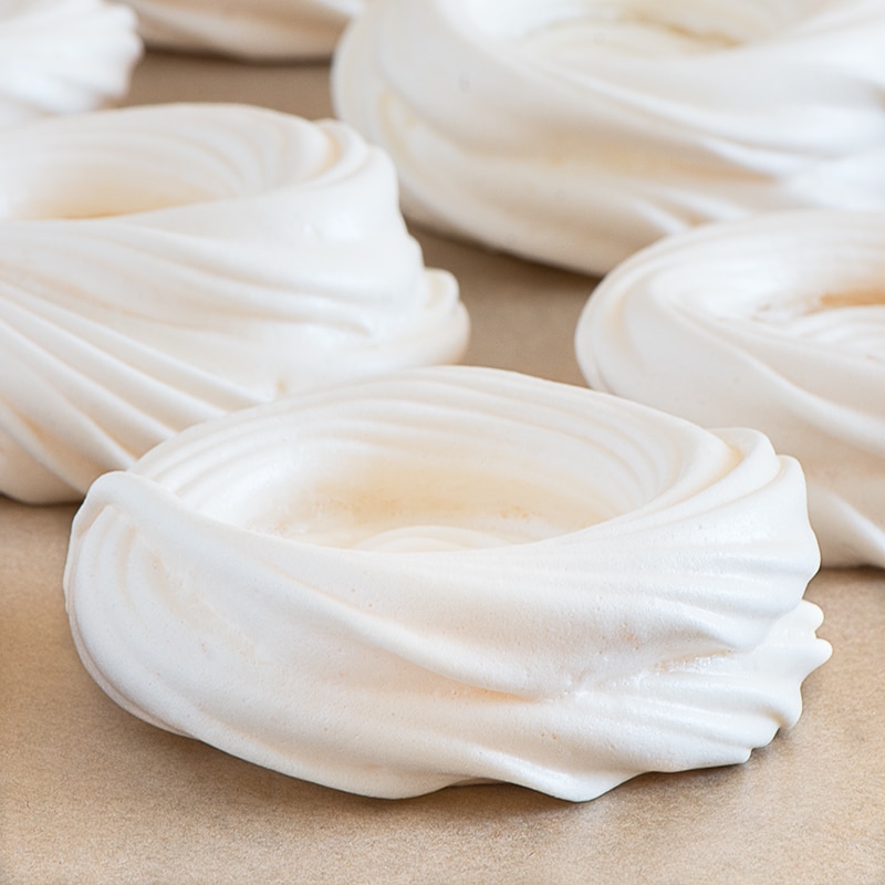 Unfilled meringue nests on a sheet of baking parchment.