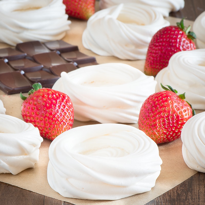 Meringue nests surrounded by fresh strawberries and a slab of dark chocolate.