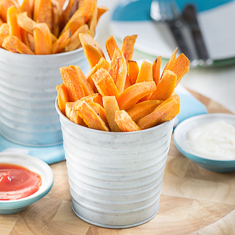 Two servings of the cooked fries stacked on their end in small metal post with ketchup and mayonnaise dipping bowls. 