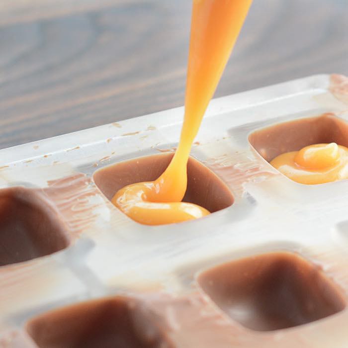 chocolatier pouring caramel filling into chocolate mold preparing handmade  candy Stock Photo - Alamy