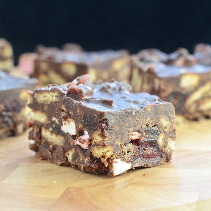 Close up of a square of rocky road sitting on a board at an angle. All the fillings are visible. 