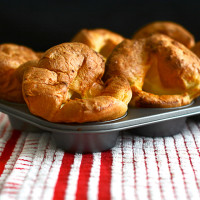 A muffin tin of perfectly risen individual Yorkshire puddings on a red and white tea towel.
