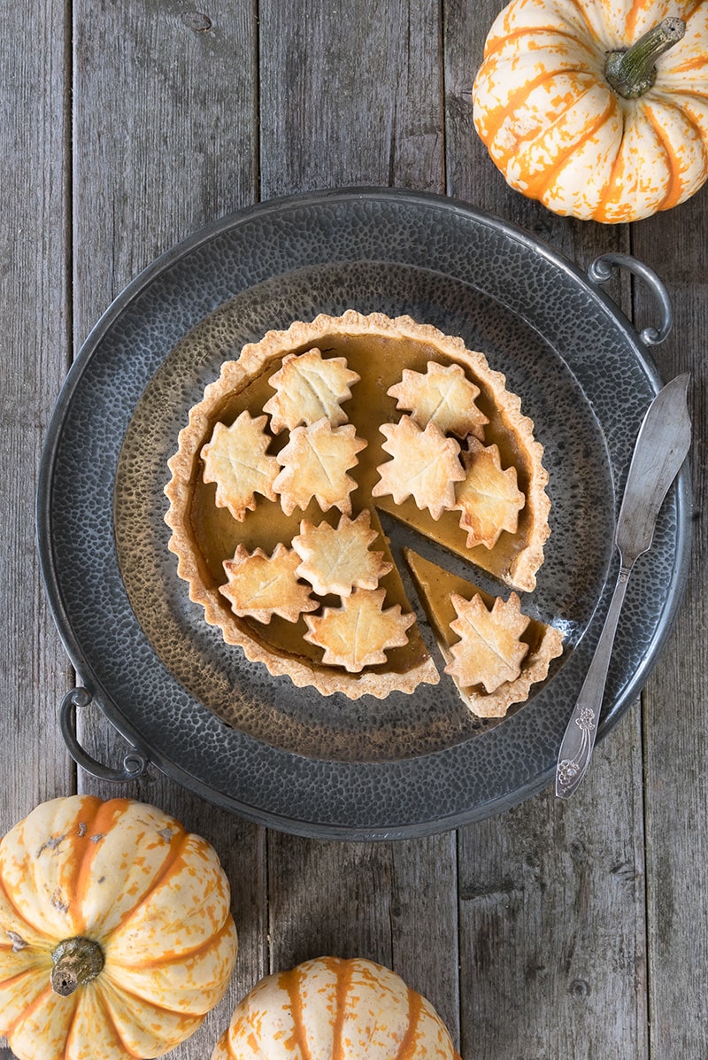 Decorated pumpkin pie shown from above with a slice partly removed. 
