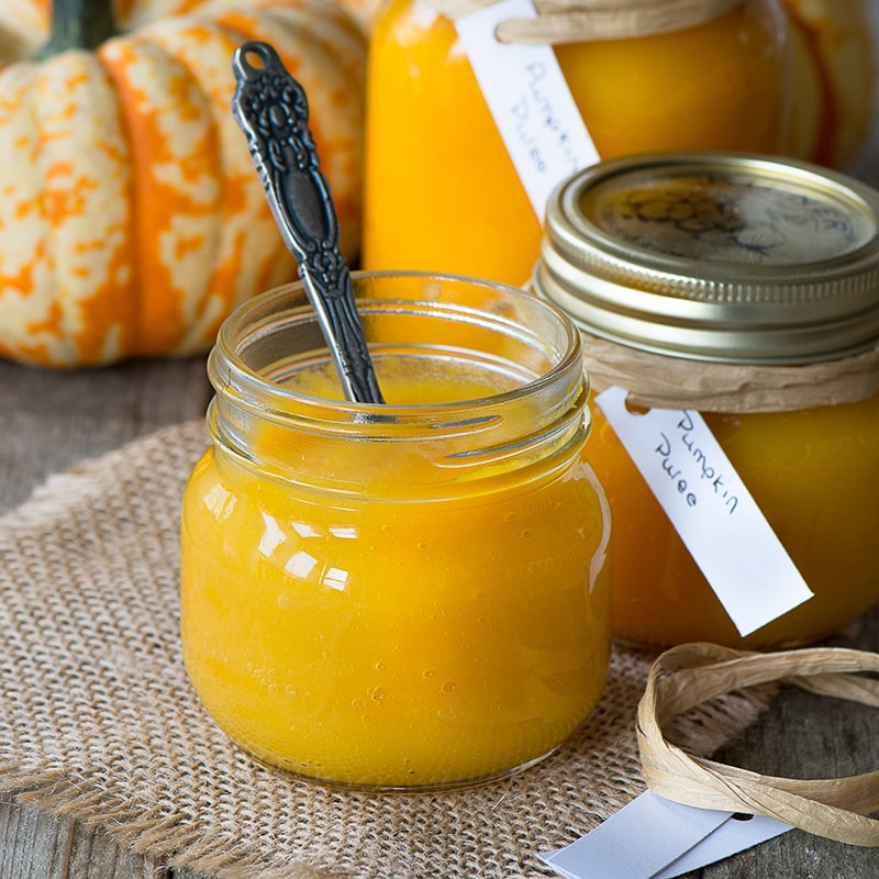 An open jar of pumpkin puree with a spoon sticking out next to another small jar with the lid on. 