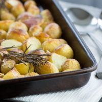Roasted new potatoes in a baking tray topped with a sprig of rosemary.