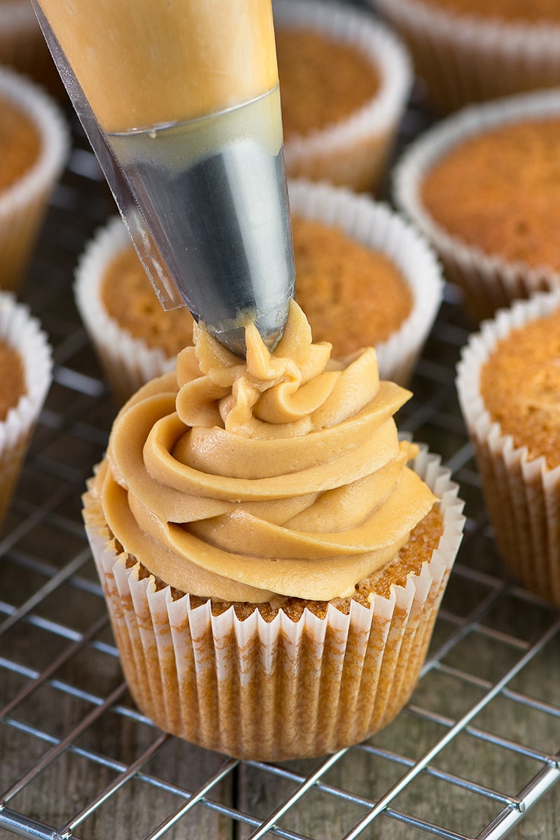 A swirl of caramel buttercream being piped onto a caramel cupcake.