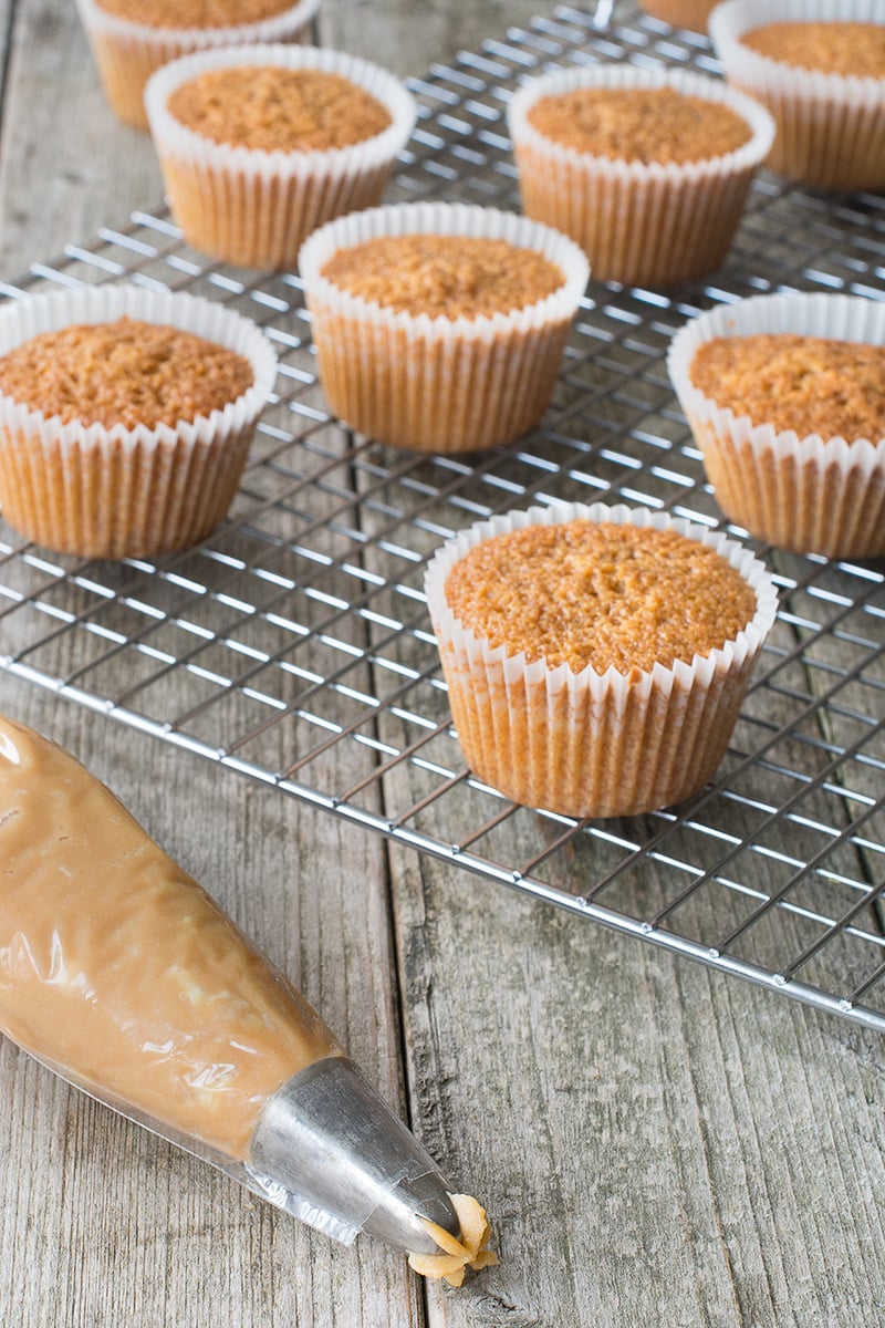 A cooling rack full of caramel cupcakes and a piping bag full of caramel buttercream ready for icing.
