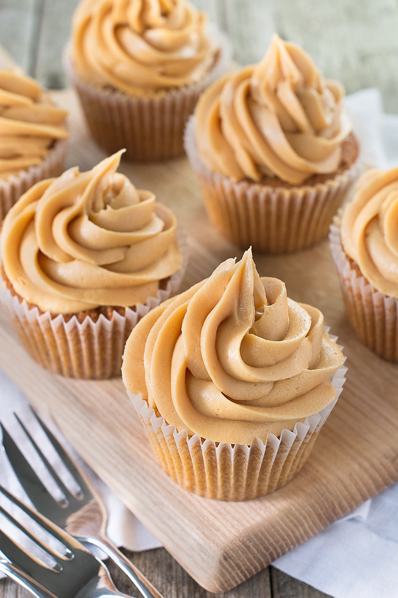 Six caramel cupcakes topped with caramel buttercream no a wooden board with cake forks. 