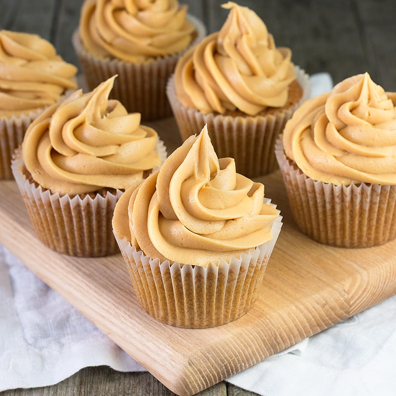 Six caramel cupcakes topped with caramel buttercream on a wooden board.