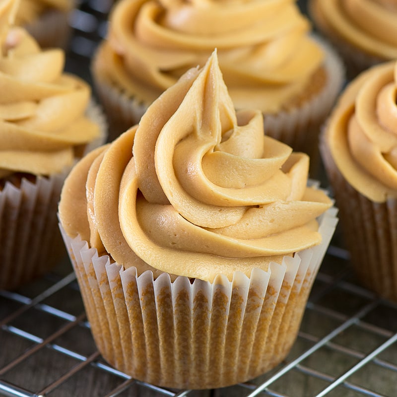 A close up of a caramel cupcake topped with a swirl of caramel buttercream with more cupcakes in the background.