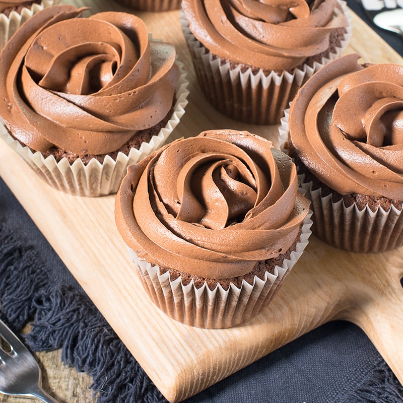 Image of chocolate cupcakes with swirls of chocolate frosting on a wooden board. 