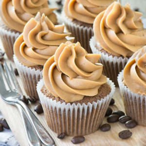 Coffee cupcakes topped with coffee buttercream on a wooden board with cake forks at the side.
