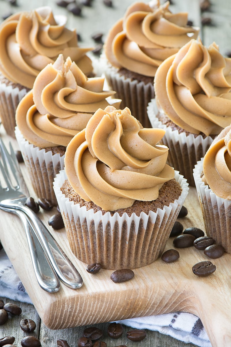 Coffee cupcakes on a wooden board with cake forks and coffee beans scattered around.
