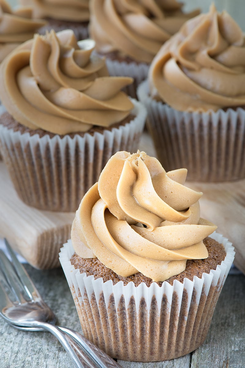 A coffee cupcake topped with coffee buttercream with a cake fork at the side and more cupcakes in the background.