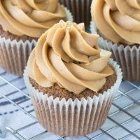 A close up of a coffee cupcake topped with a swirl of coffee buttercream on a cooling rack with more cupcakes behind.