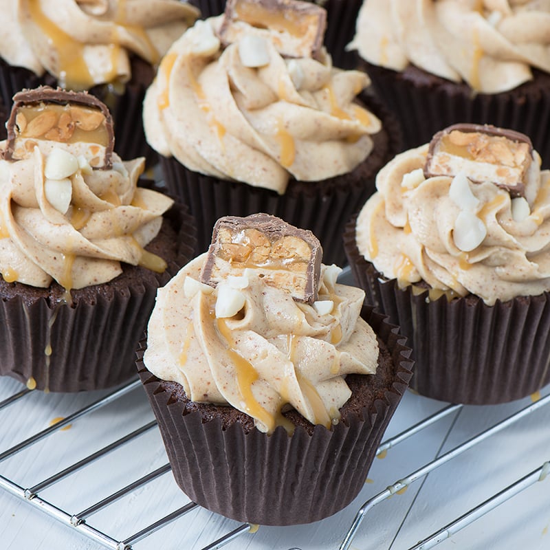 Snickers Cupcakes - Chocolate Cupcakes filled with caramel sauce and topped with smooth peanut buttercream, more caramel, crunchy peanuts and a little slice of Snickers.