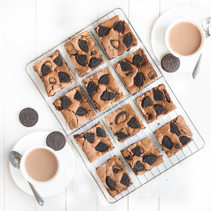 A top-down view of peanut butter Oreo brownies on a cooling rack. Next to the rack is two cups of tea.
