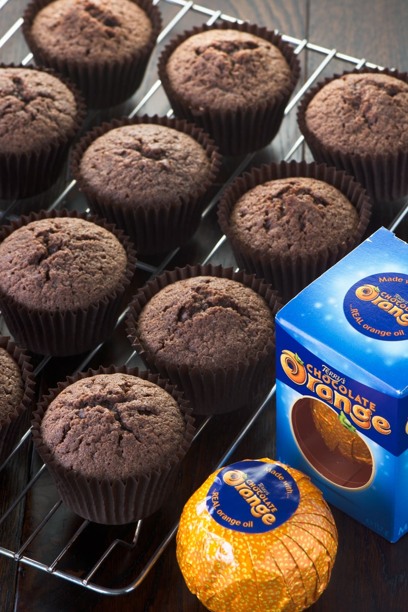 Chocolate orange cupcakes on a cooling rack with a box of chocolate orange at the side.