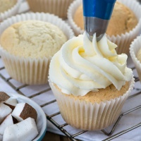Coconut buttercream being piped onto a coconut cupcake.
