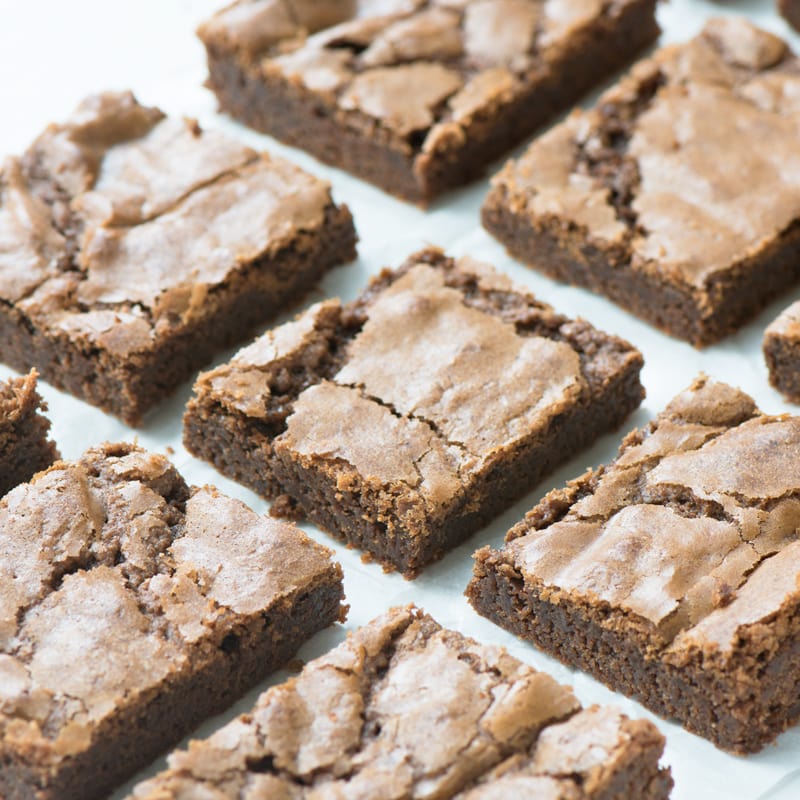 Homemade chocolate brownies cut into squares and arranged in rows. You can see the crisp, shiny top and gooey centre.