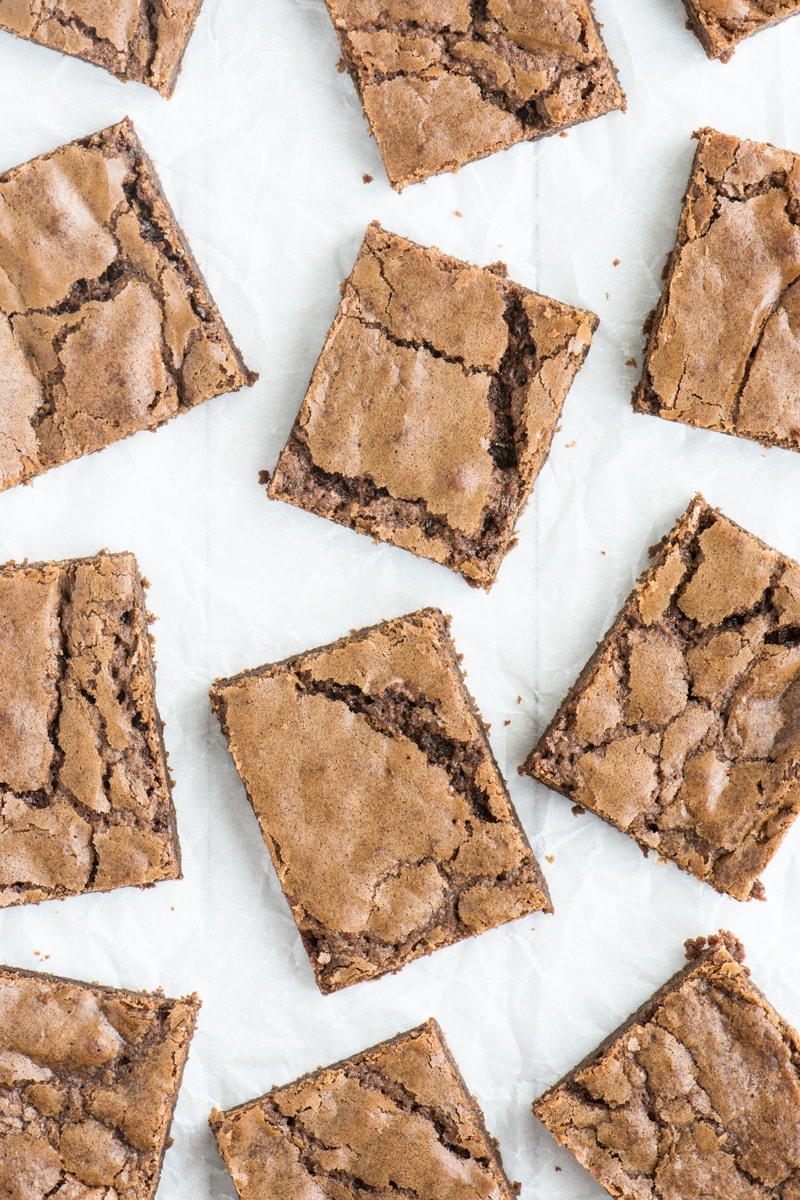 Looking down on a batch of easy homemade chocolate brownies cut into squares and arranged randomly on a white background.