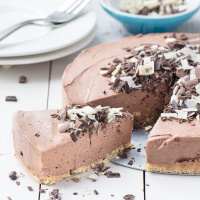 A slice of no-bake chocolate cheesecake next to the remaining cheesecake covered with dark and white chocolate curls.