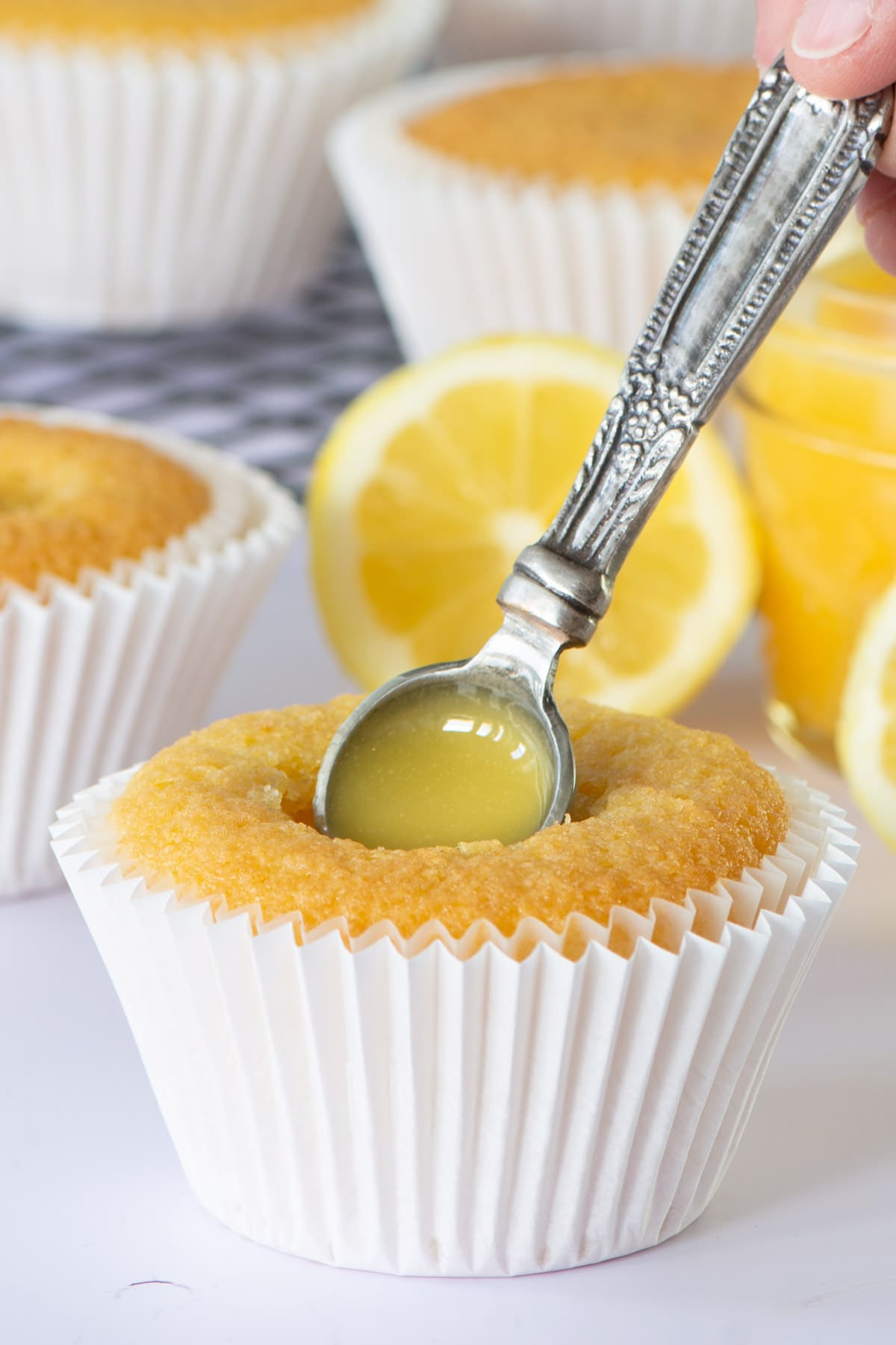 A lemon cupcake being filled with a hidden lemon curd centre. There are other cupcakes and cut lemons in the centre.