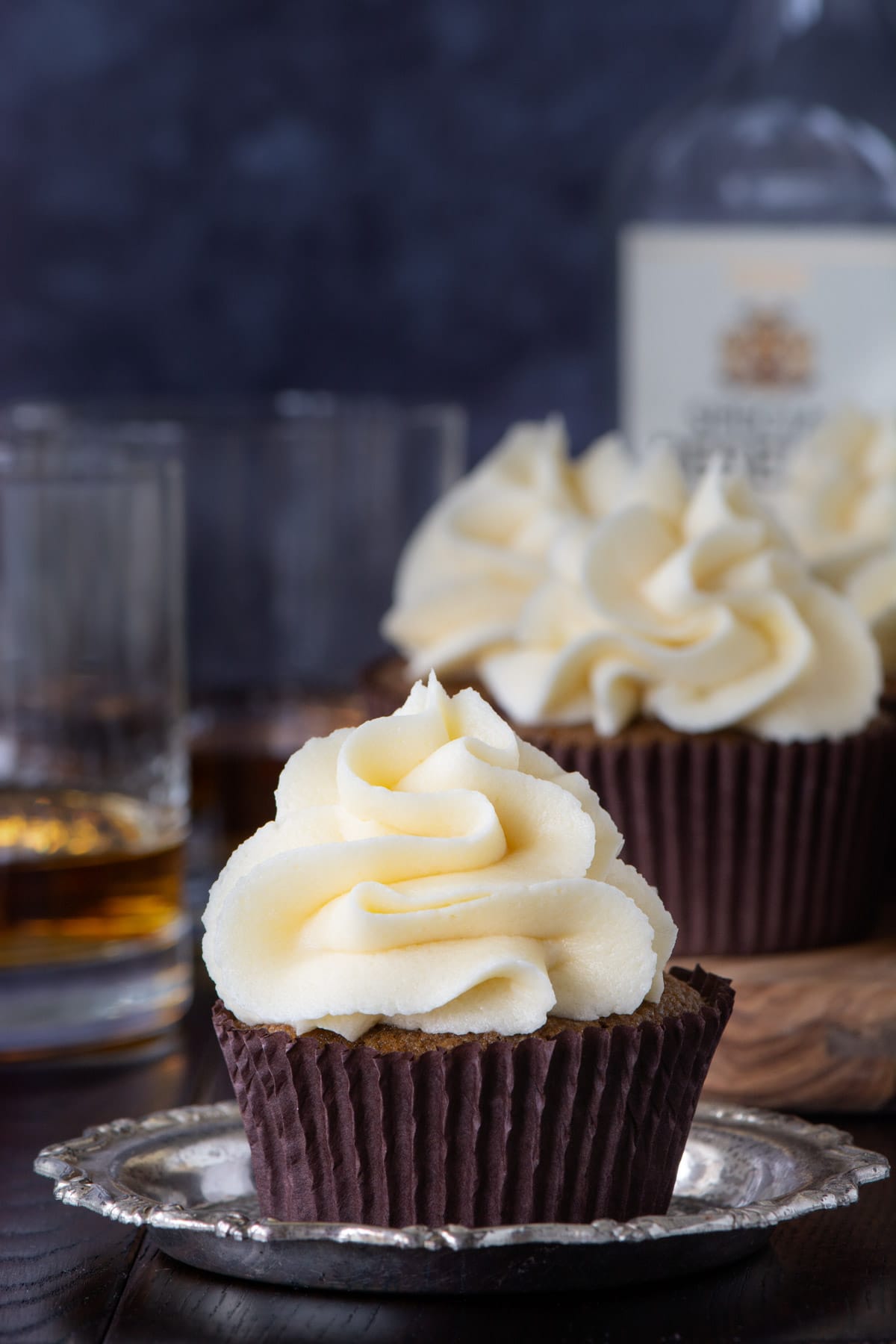 A close up of a coffee cupcakes topped with whiskey buttercream. There are more cupcakes in the background.