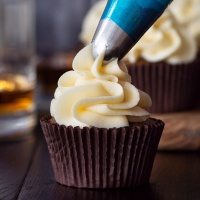Whisky buttercream being piped onto a coffee cupcake.