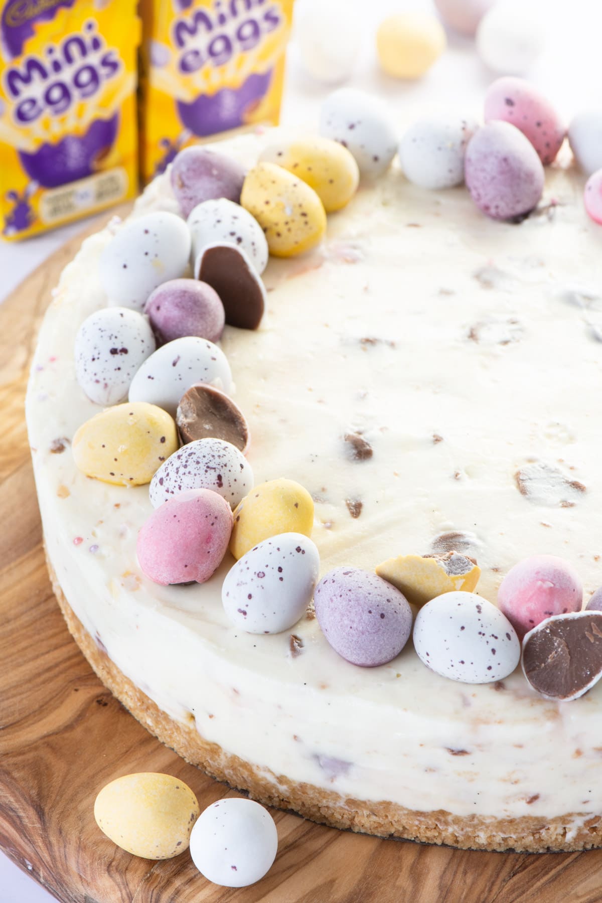 A white chocolate mini egg cheesecake with boxes of mini eggs in the background.