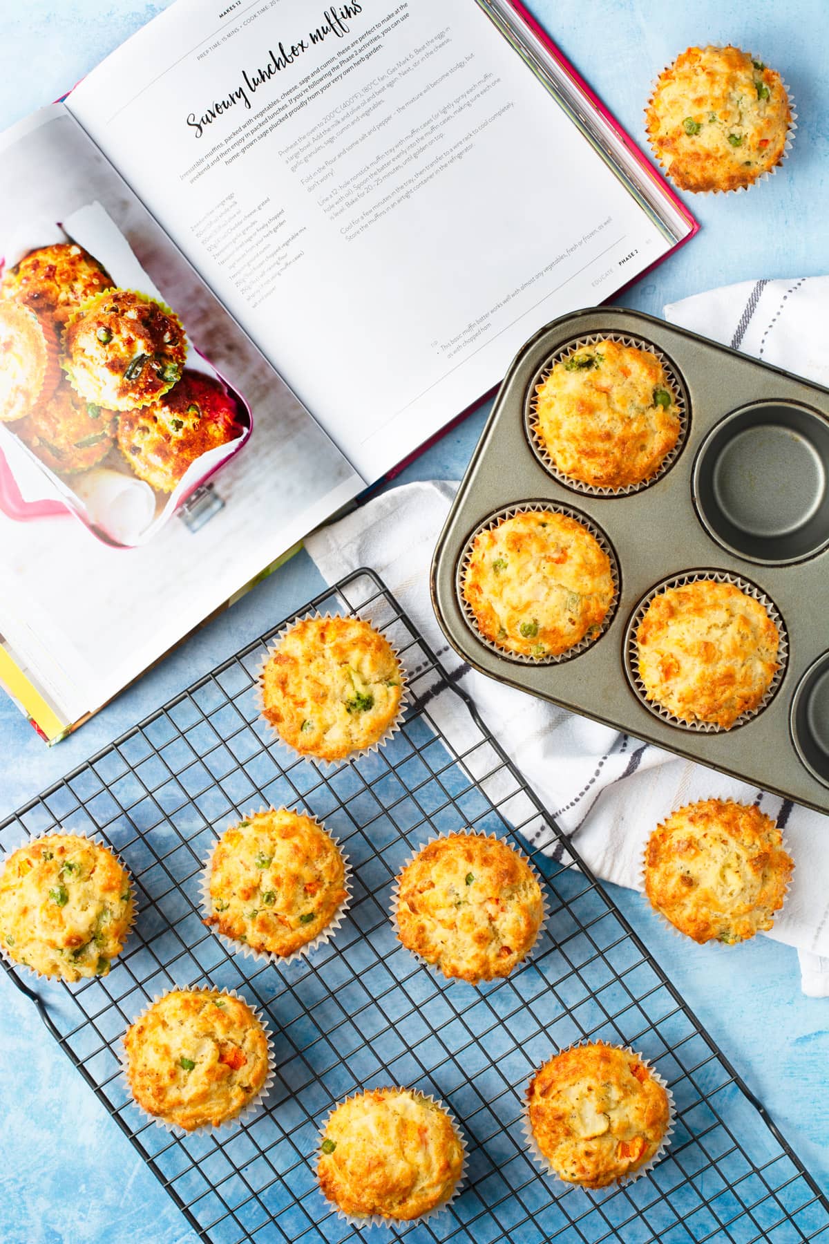 Savoury muffins in a muffin tin and on a cooling rack. The cookbook is open on the recipe page showing the original recipe.