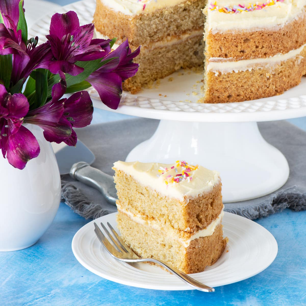 A slice of vegan vanilla cake with the rest of the cake in the background.