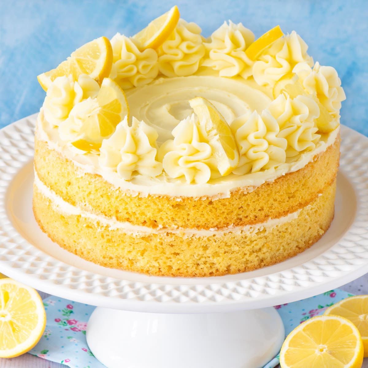 Lemon cake topped with lemon buttercream on a white cake stand.