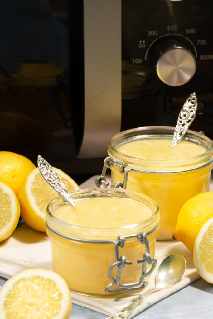 Two jars of lemon curd in front of a microwave.