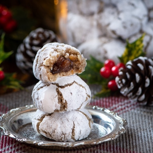 A stack of three Christmas Amaretti Biscuits on a silver dish. The top biscuits is cut in half showing the hidden mincemeat centre.
