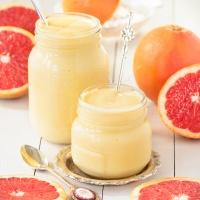 Two jars of grapefruit curd surrounded by cut pink grapefruits